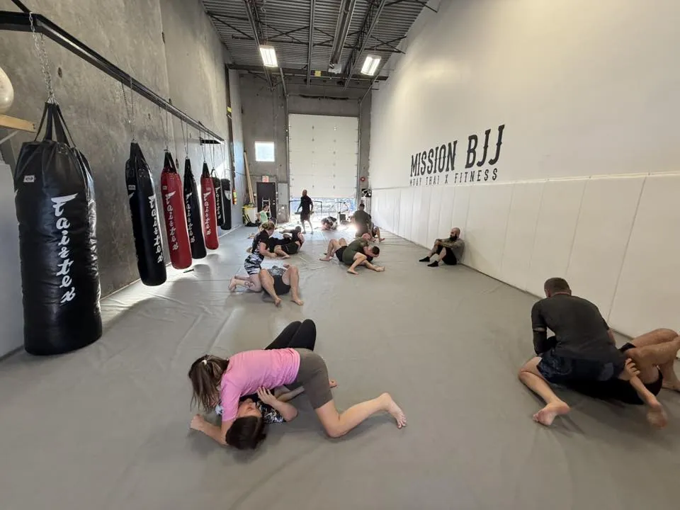 Members grappling across the open mats of the Mission BJJ training floor